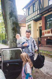 Father carrying son and bag while looking girl entering car