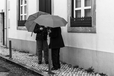 Friends with umbrellas standing on footpath by house