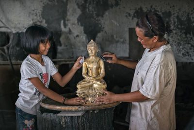 Smiling daughter and mother cleaning buddha statue