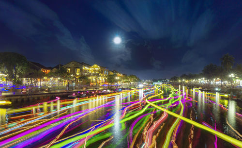 Light trails on illuminated city against sky at night