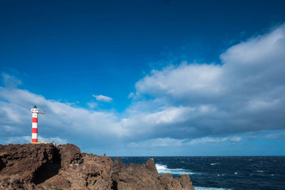 Lighthouse by sea against blue sky