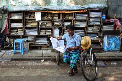 Full length of disabled man reading newspaper while sitting on tricycle