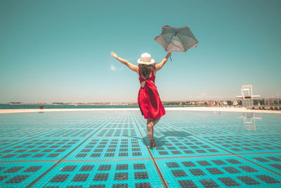 Rear view of woman standing by swimming pool against sky