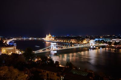 Illuminated bridge over river in city at night