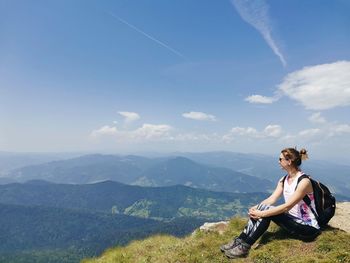 Woman sitting on mountain against sky