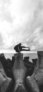 Man on rock by sea against sky