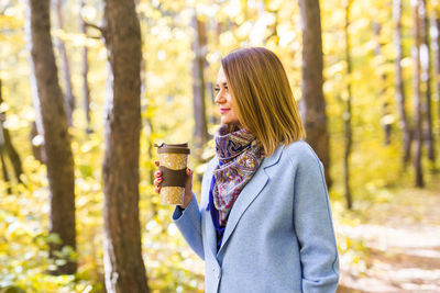 Woman standing by tree trunk in forest