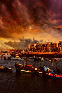 Boats moored in sea by buildings against sky during sunset