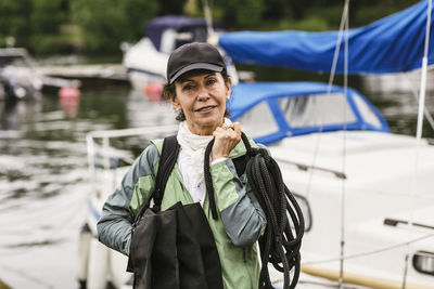 Portrait of confident female instructor holding rope and life jackets against yacht during boat master course