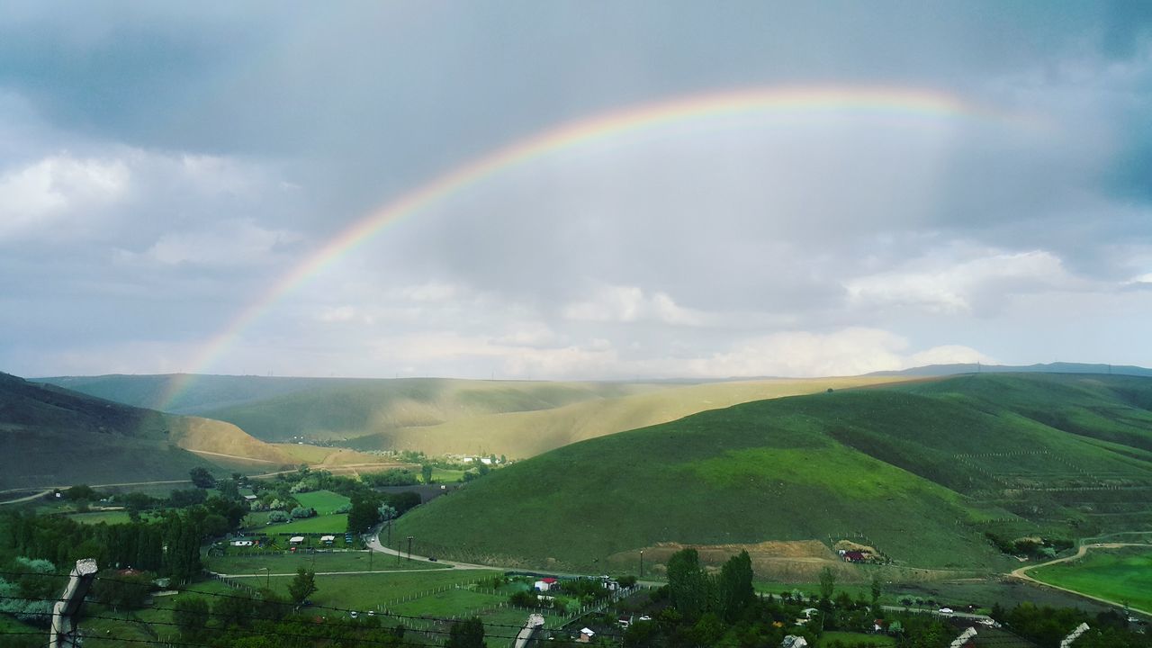 rainbow, multi colored, beauty in nature, scenics, tranquil scene, landscape, tranquility, mountain, nature, arch, idyllic, town, natural arch, majestic, cloud, mountain range, sky, remote, day, natural phenomenon, cloud - sky, rural scene, lush foliage, outdoors, non-urban scene, storm cloud, solitude