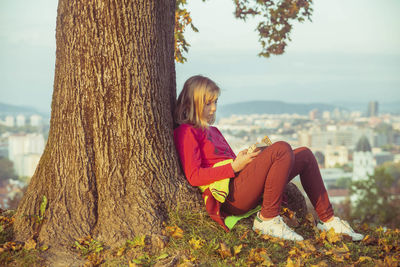 Teenage girl sitting under an autumn tree on a hill on the sunset