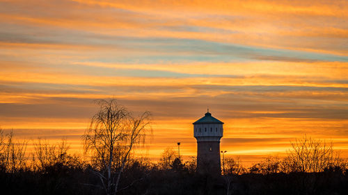 Silhouette tower by building against orange sky