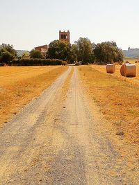 Dirt road amidst field against clear sky