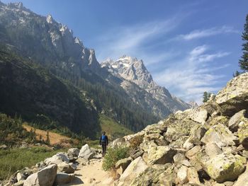 Rear view of man walking on rocky mountain against sky