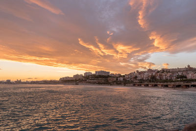 Scenic view of sea by buildings against sky during sunset