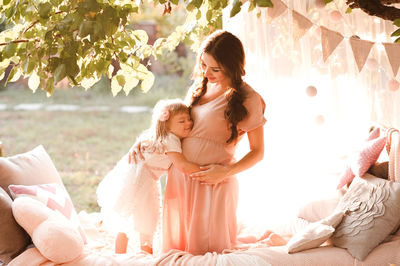 Smiling daughter embracing pregnant mother on bed