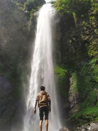 Rear view of man standing against waterfall