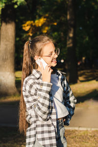 Cheerful girl in glasses talking on a dump phone outside vertical view