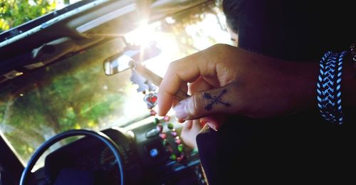 Cropped tattooed hand of man holding marijuana joint in car