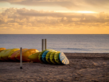 Deck chairs on beach against sky during sunset