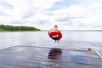 Boy jumping in a red lifebuoy from the bridge into the river, lake. life style. summer 