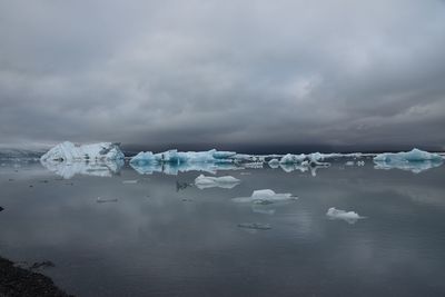 Scenic view of glaciers on lagoon against cloudy sky