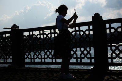 Silhouette woman standing by railing against sky