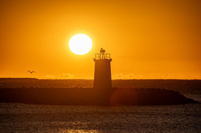 Lighthouse by sea against sky during sunset