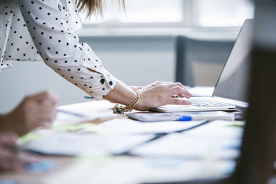 Cropped hands of businesswoman using laptop computer with colleague in board room