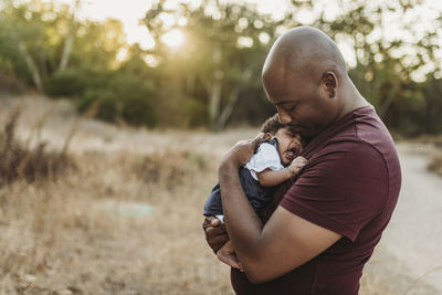 Close up of sweet father cuddling newborn girl in backlit field