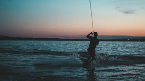 Silhouette of a man doing wakeboarding in a lake with mountains in the background