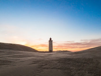 Lighthouse on beach against sky during sunset