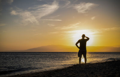 Silhouette man standing on beach against sky during sunset