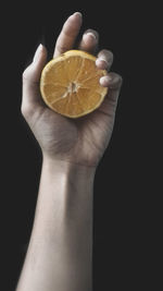 Cropped hand of woman holding orange against black background