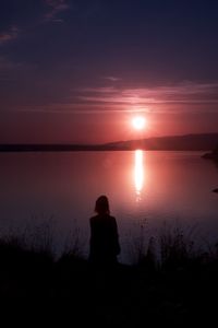 Silhouette of woman against colorful sunset over lake 