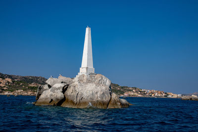 Lighthouse by sea against clear blue sky