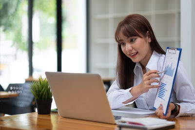 Young woman using phone while sitting on table