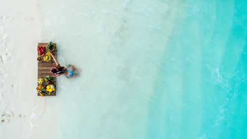 High angle view of young woman wearing bikini with fruits on wooden raft in sea