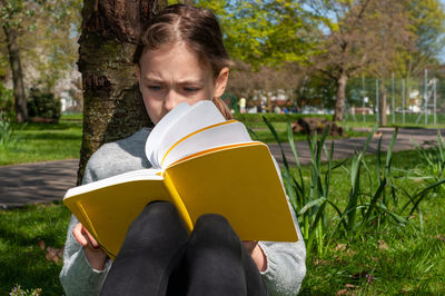 Portrait of young woman reading book while sitting on field