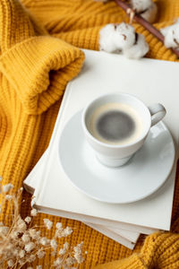 Cozy composition of warm yellow sweater, white books , cup of hot coffee and dry flowers 