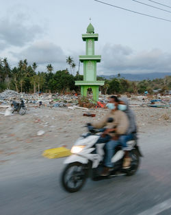 People riding motorcycle on road against sky in city