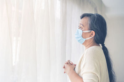 Side view portrait of woman wearing mask standing against window