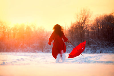 A girl in red with a red umbrella runs across the field.