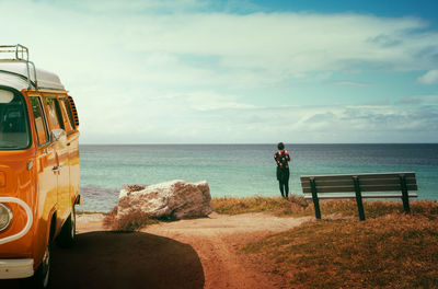 Rear view of woman standing by sea against sky