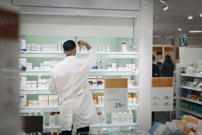 Rear view of male pharmacist arranging medicines on rack at store