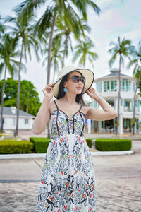 Portrait of young woman standing against palm trees