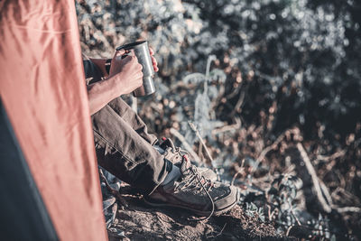 Low section of man drinking coffee while sitting on rock