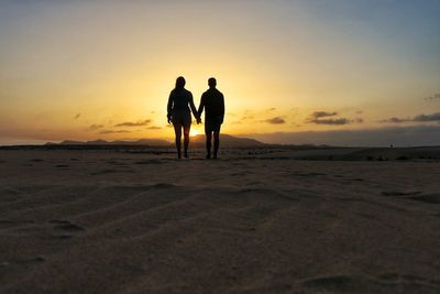 Silhouette couple on beach against sky during sunset