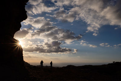 Silhouette people standing on rock against sky during sunset