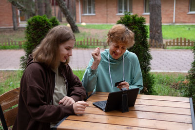 Portrait of smiling friends sitting on bench at park